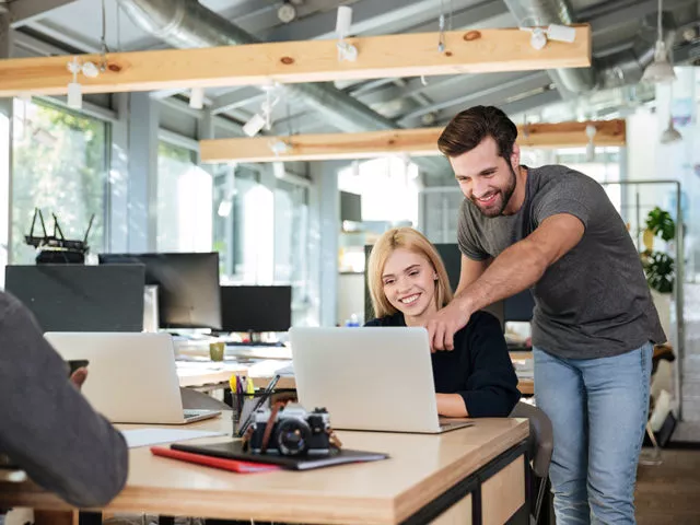 Picture of cheerful young colleagues sitting in office coworking using laptop computers. Looking aside.